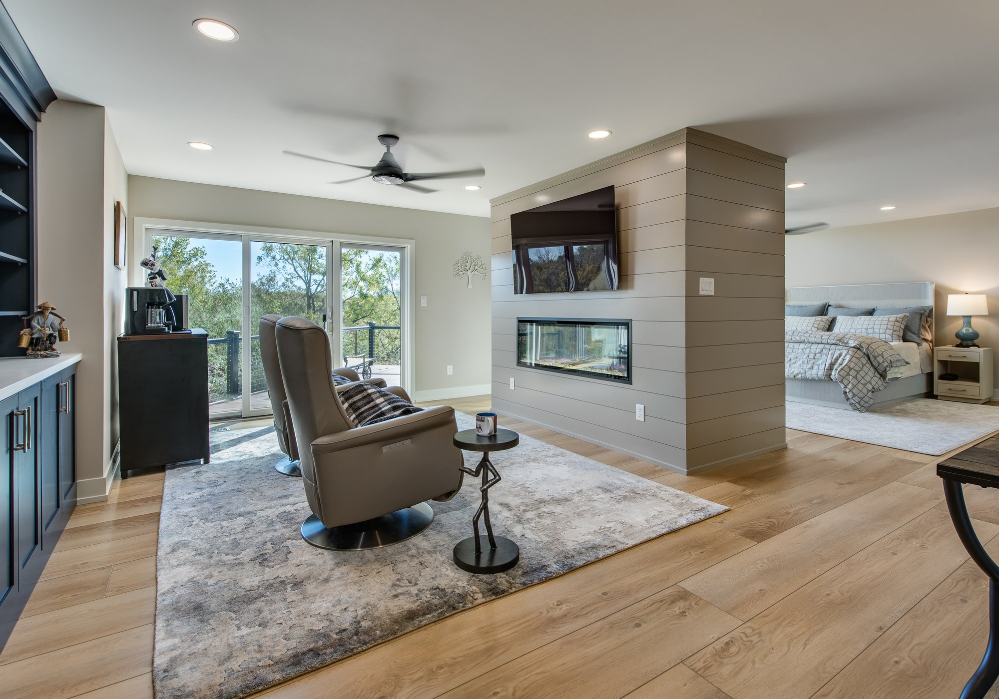 A primary bedroom remodel with a custom room divider with a mounted TV facing a set of recliners
