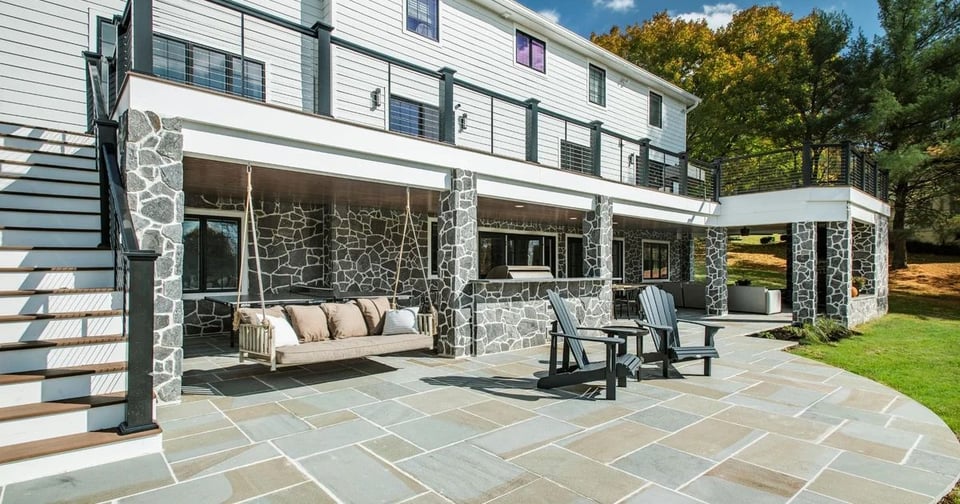 Two-story outdoor living area with stone pillars, porch swing, and open backyard seating