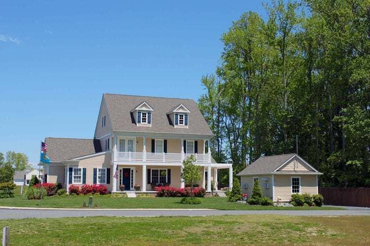 Custom-built two-story home with a large front porch, dormer windows, and a detached garage, surrounded by lush greenery in a suburban setting - Thompson Communities - Chester County Builder and Remodeler 
