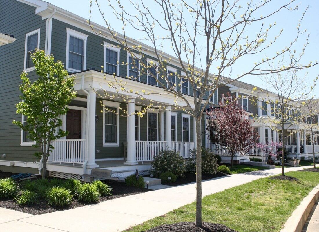 Row of green custom townhomes by Thompson Communities in West Chester, PA, with blooming spring trees