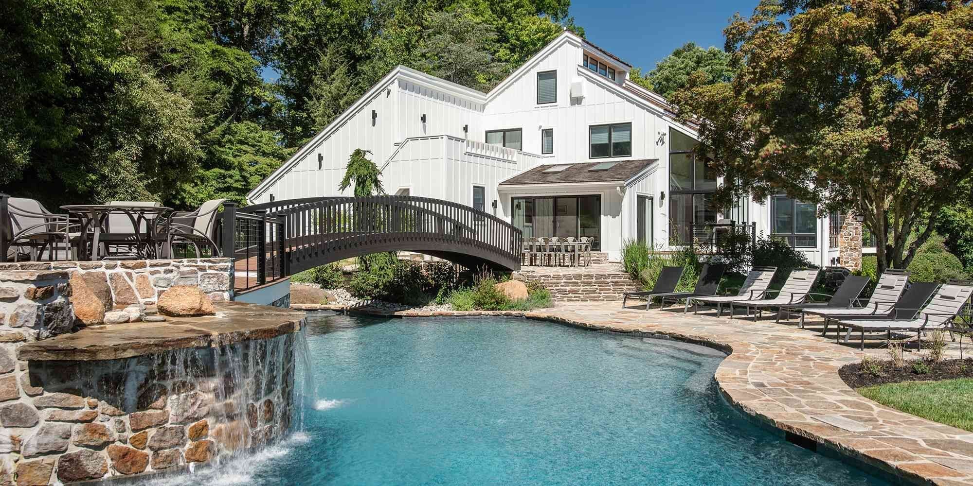 A custom home hardscaping with pool, stone patio, and bridge in West Chester, PA by Thompson Communities