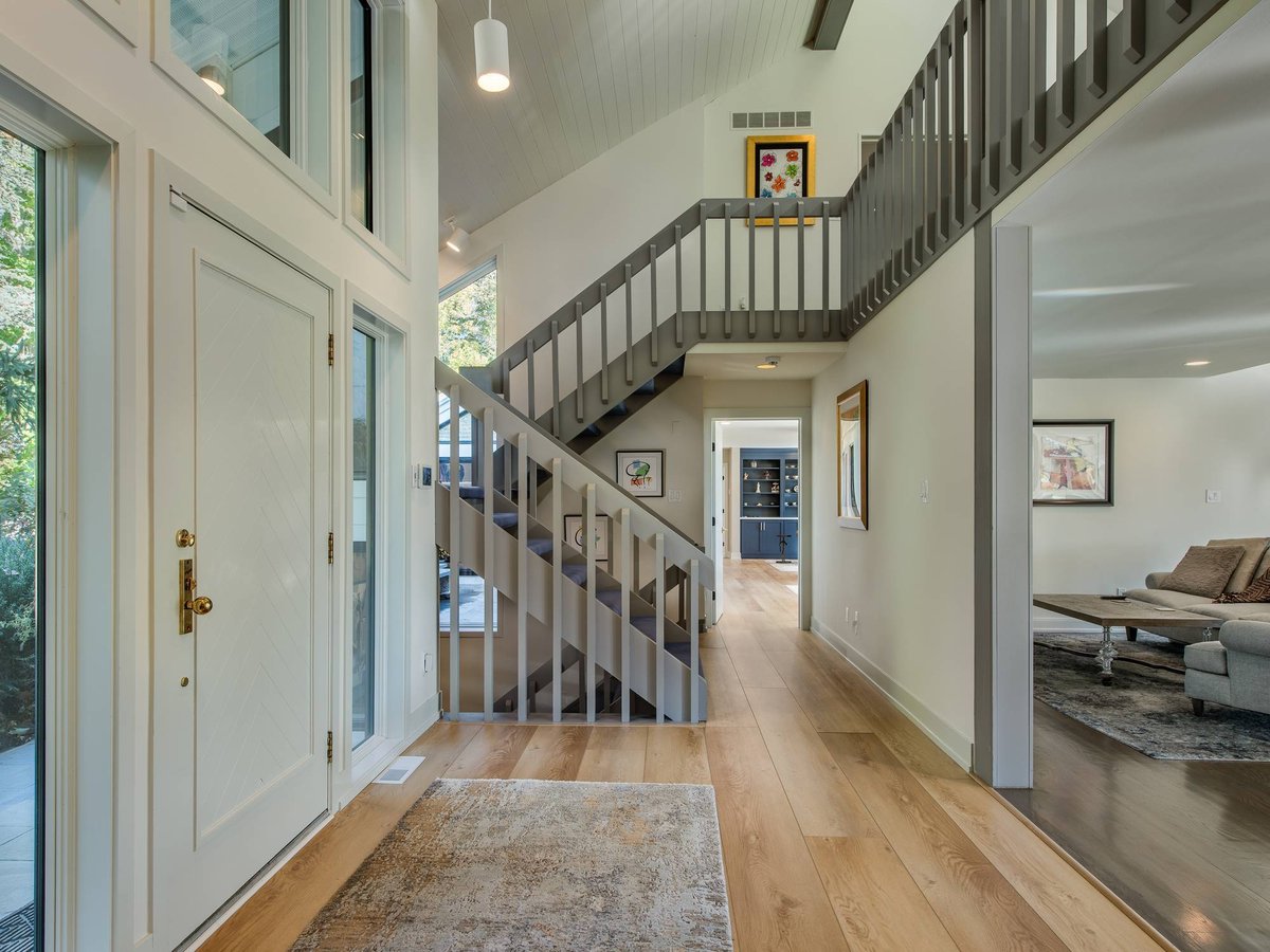 Bright entryway with vaulted ceiling, gray staircase, wide-plank hardwood floors, and glass front door