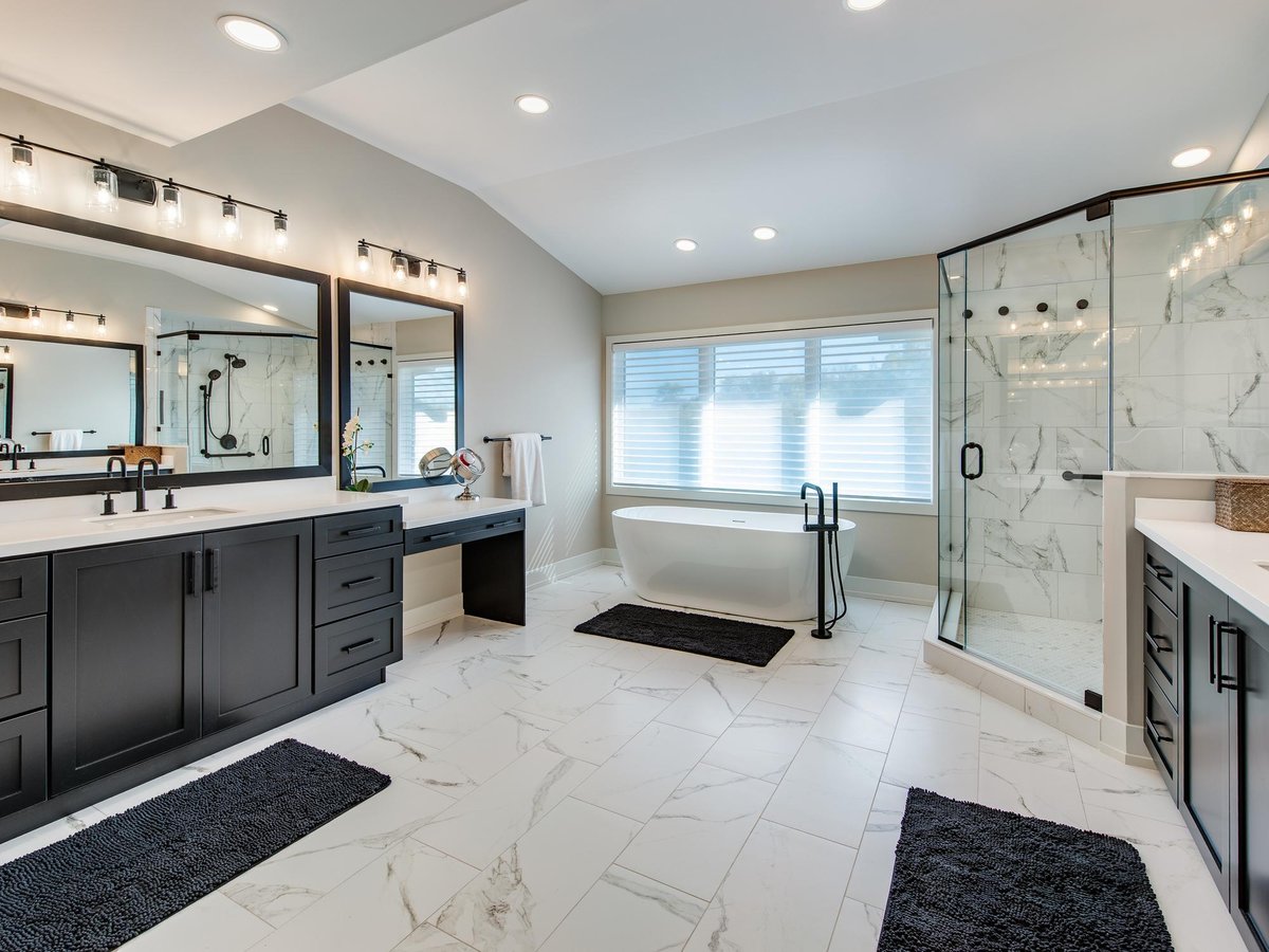Primary bathroom remodel with dark double vanity, freestanding soaking tub, and glass-walled marble tile shower