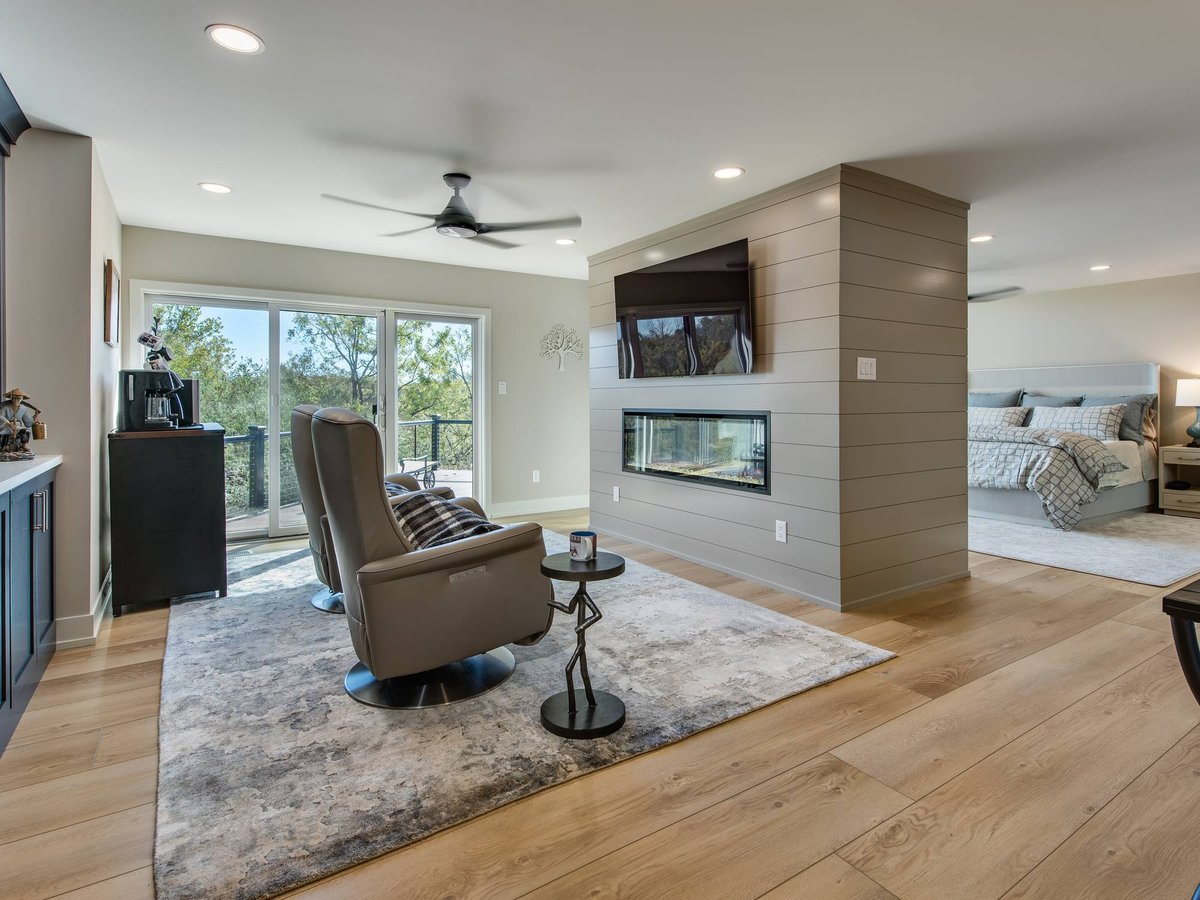 Primary bedroom sitting area with a two-sided fireplace, mounted TV, and pair of leather recliners on a plush rug