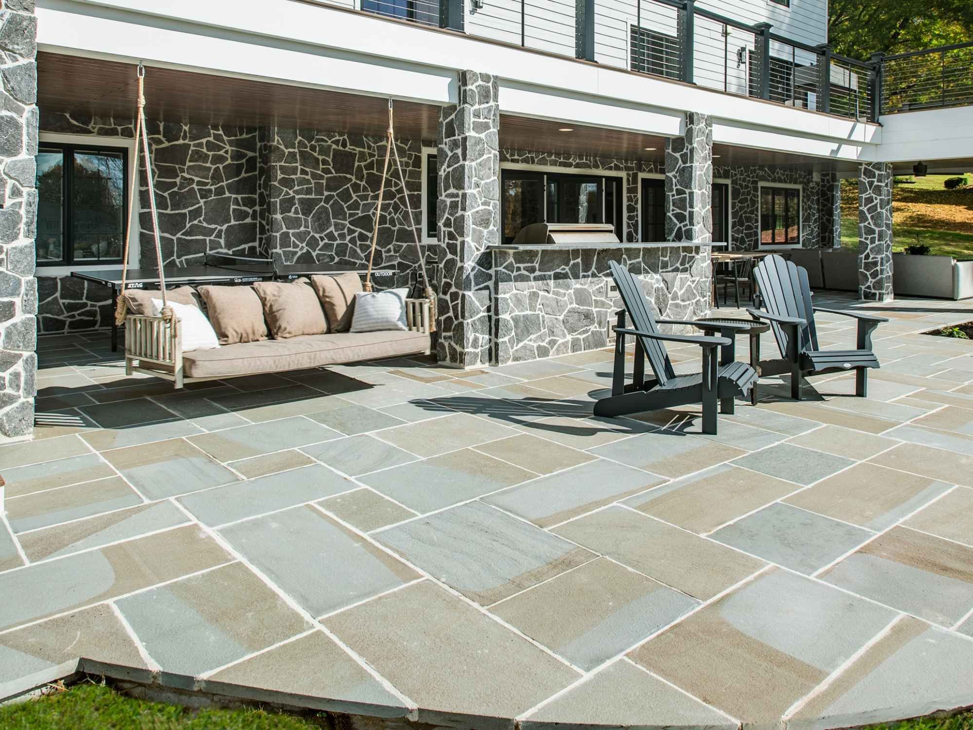 Two-story outdoor living area with stone pillars, porch swing, and open backyard seating in West Chester, PA by Thompson Communities Two-story outdoor living area with stone pillars, porch swing, and open backyard seating in West Chester, PA by Thompson Communities