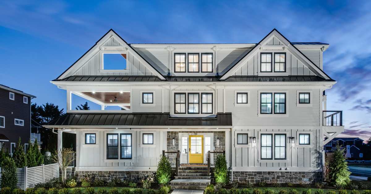 [FI]Front view of an Avalon custom home at dusk with a black metal standing seam roof, white Hardie siding, and Pennsylvania blue flagstone around the entrance by Thompson Communities
